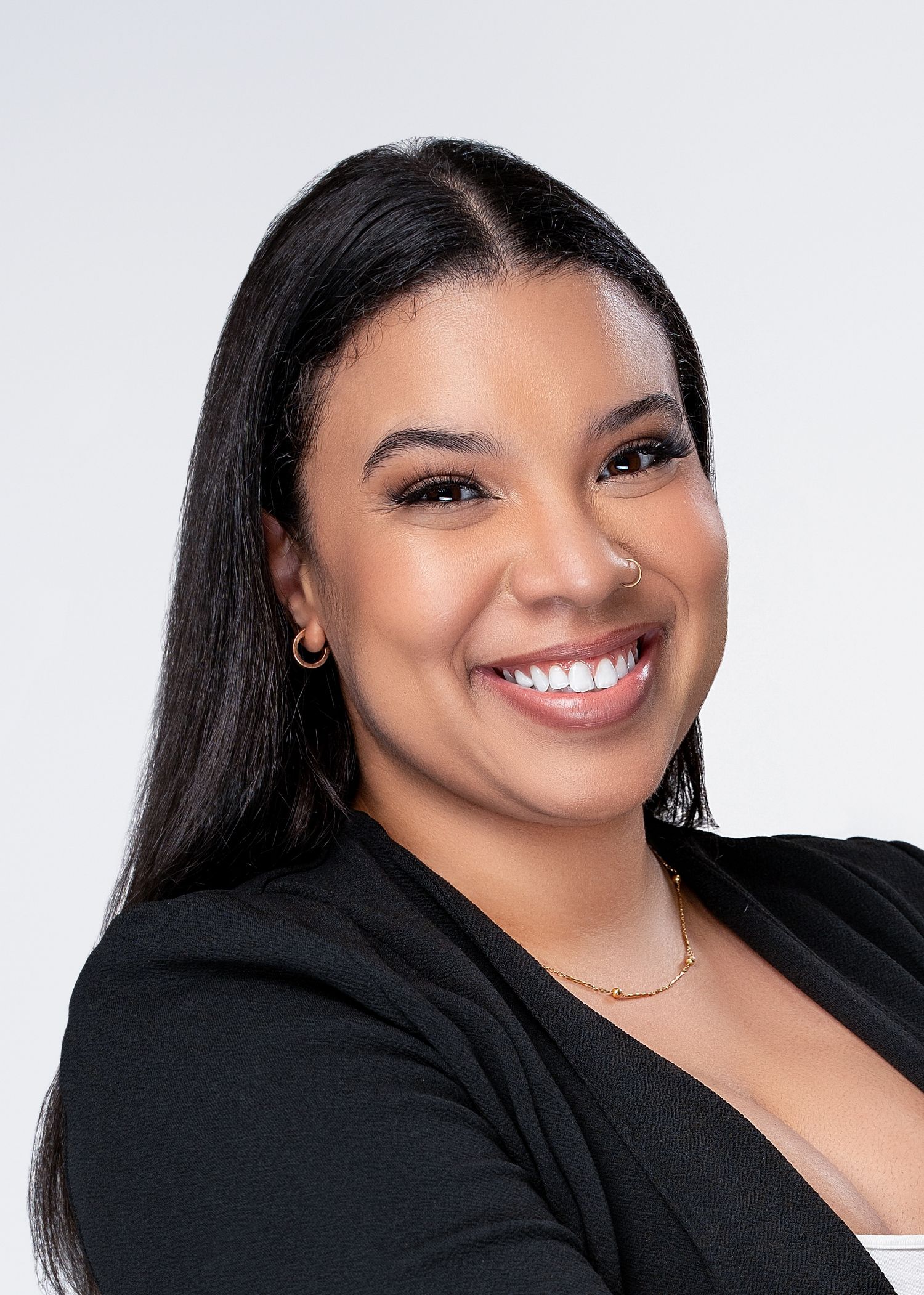 Professional headshot of person in black blazer smiling warmly against light background.