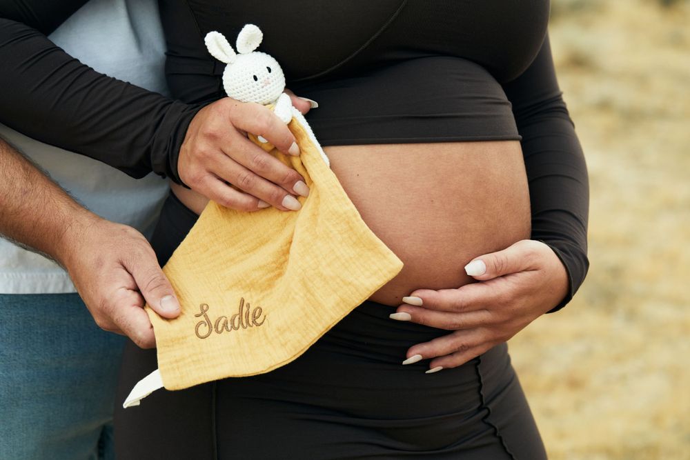 Close-up of hands holding yellow baby blanket with bunny toy during maternity shoot.
