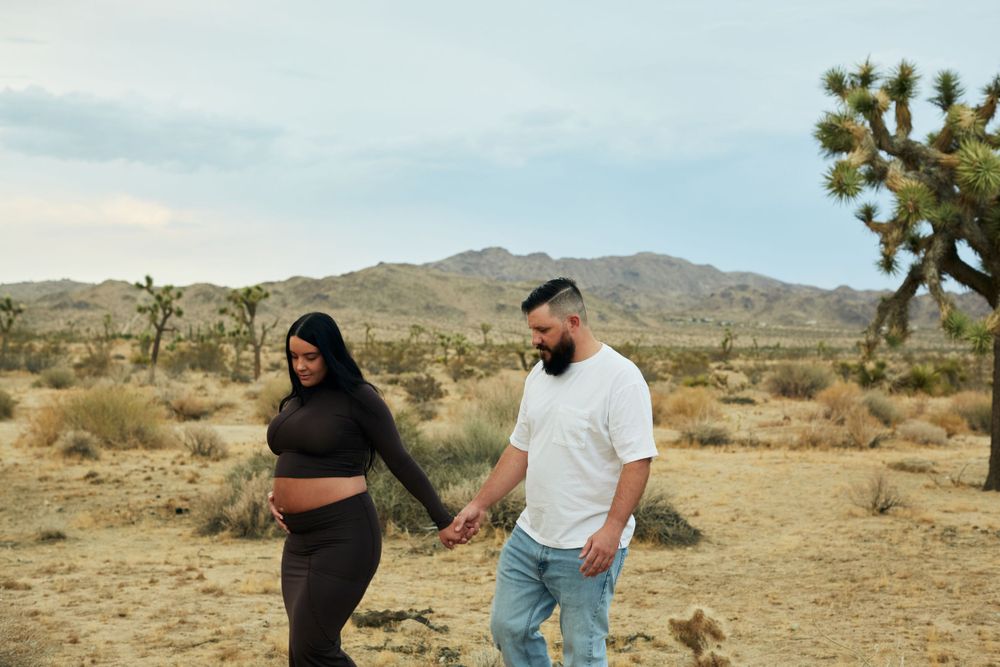Couple walking hand in hand through desert landscape with Joshua trees in background.