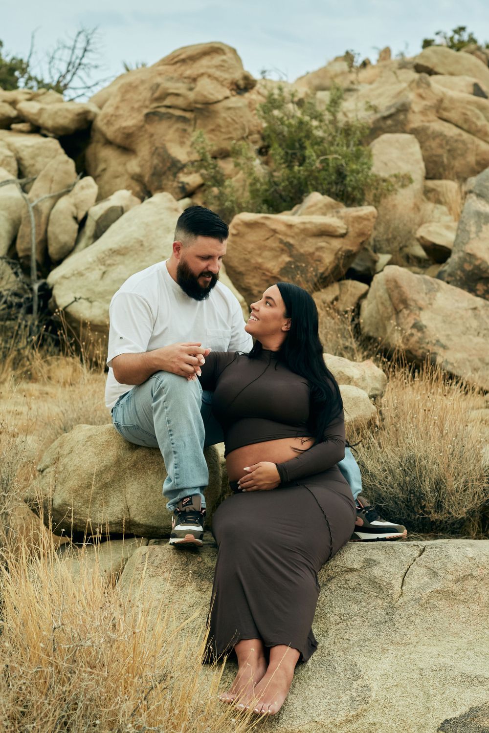 Couple sharing a tender moment while sitting on desert rocks during golden hour.