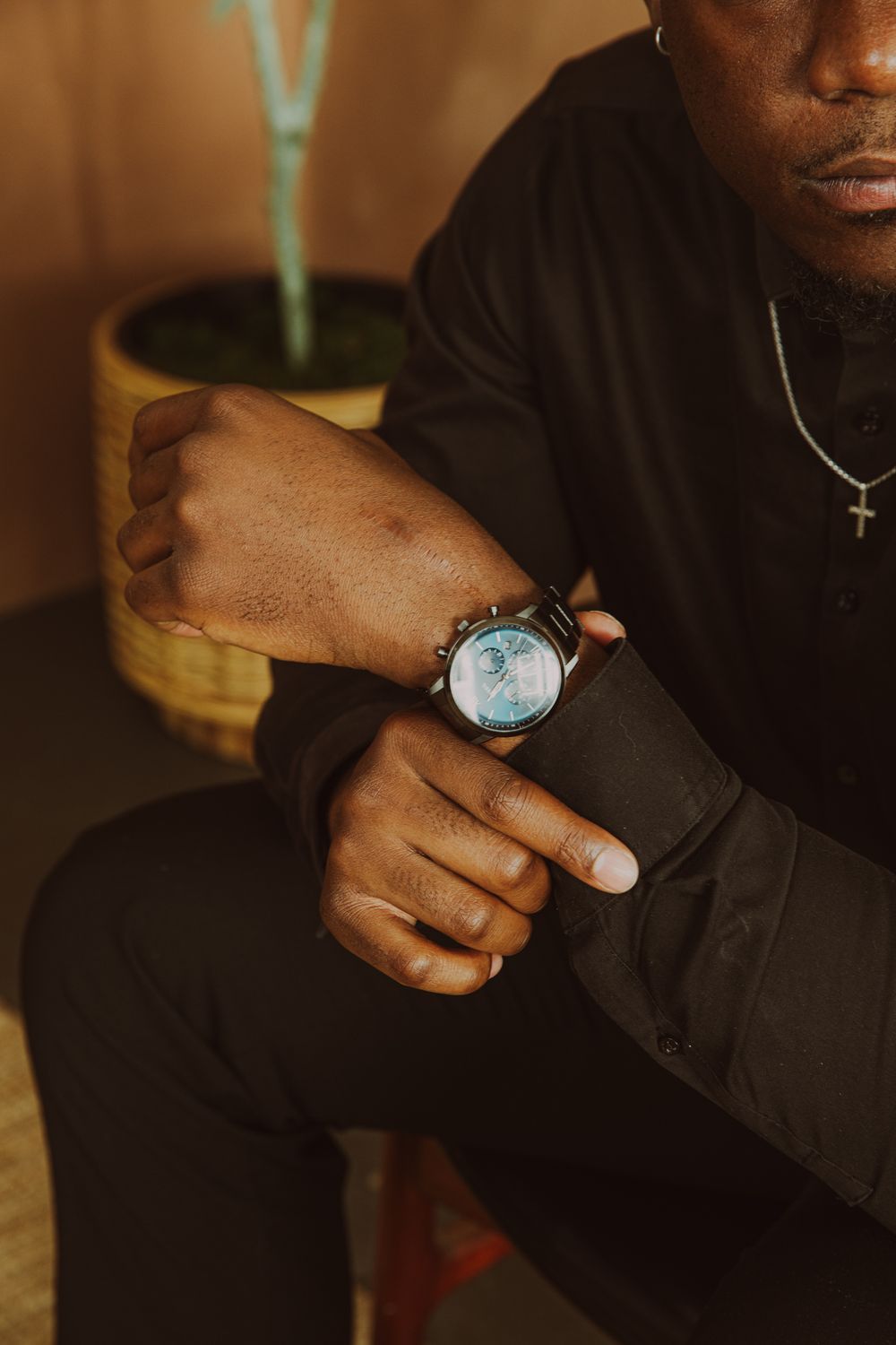 Close-up of Black man in all-black outfit adjusting a stylish watch on his wrist.