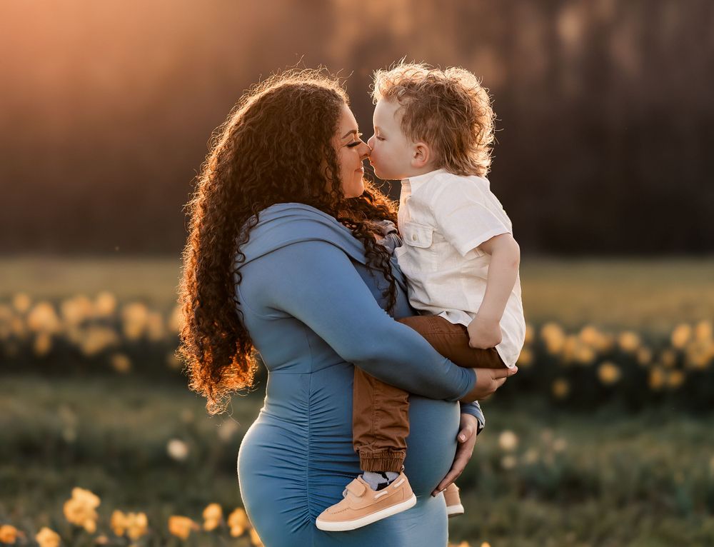A couple embraces in a golden field at sunset surrounded by spring flowers.
