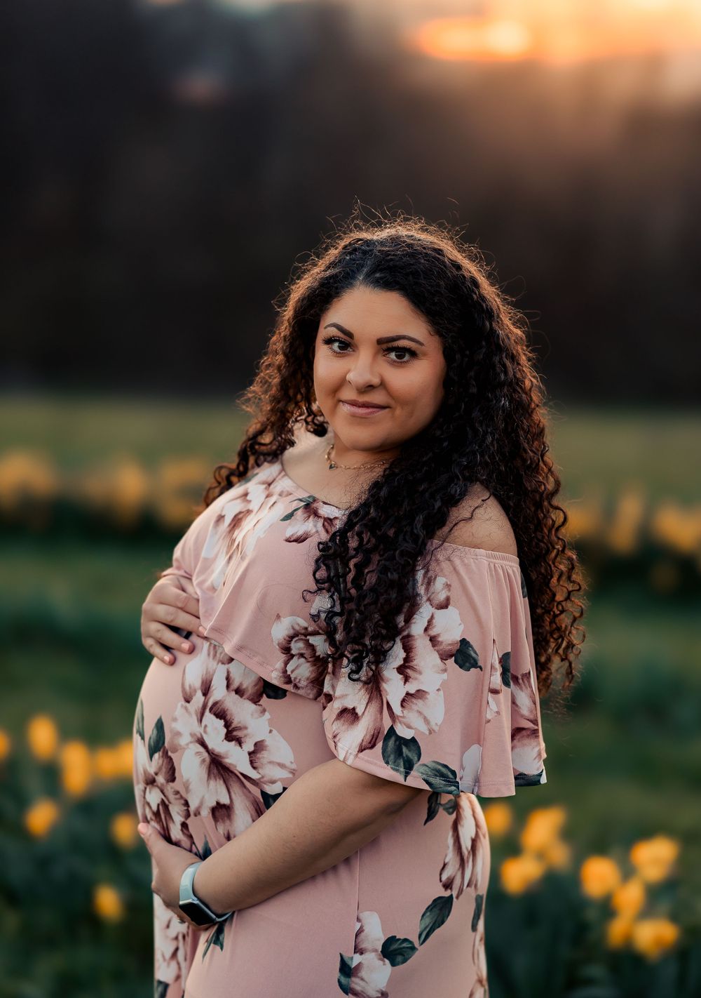 Woman in floral dress poses joyfully in a spring meadow at sunset.