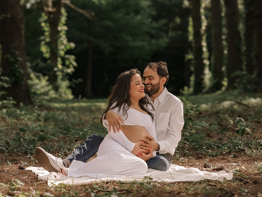 Couple sits on white blanket during intimate forest maternity photoshoot.