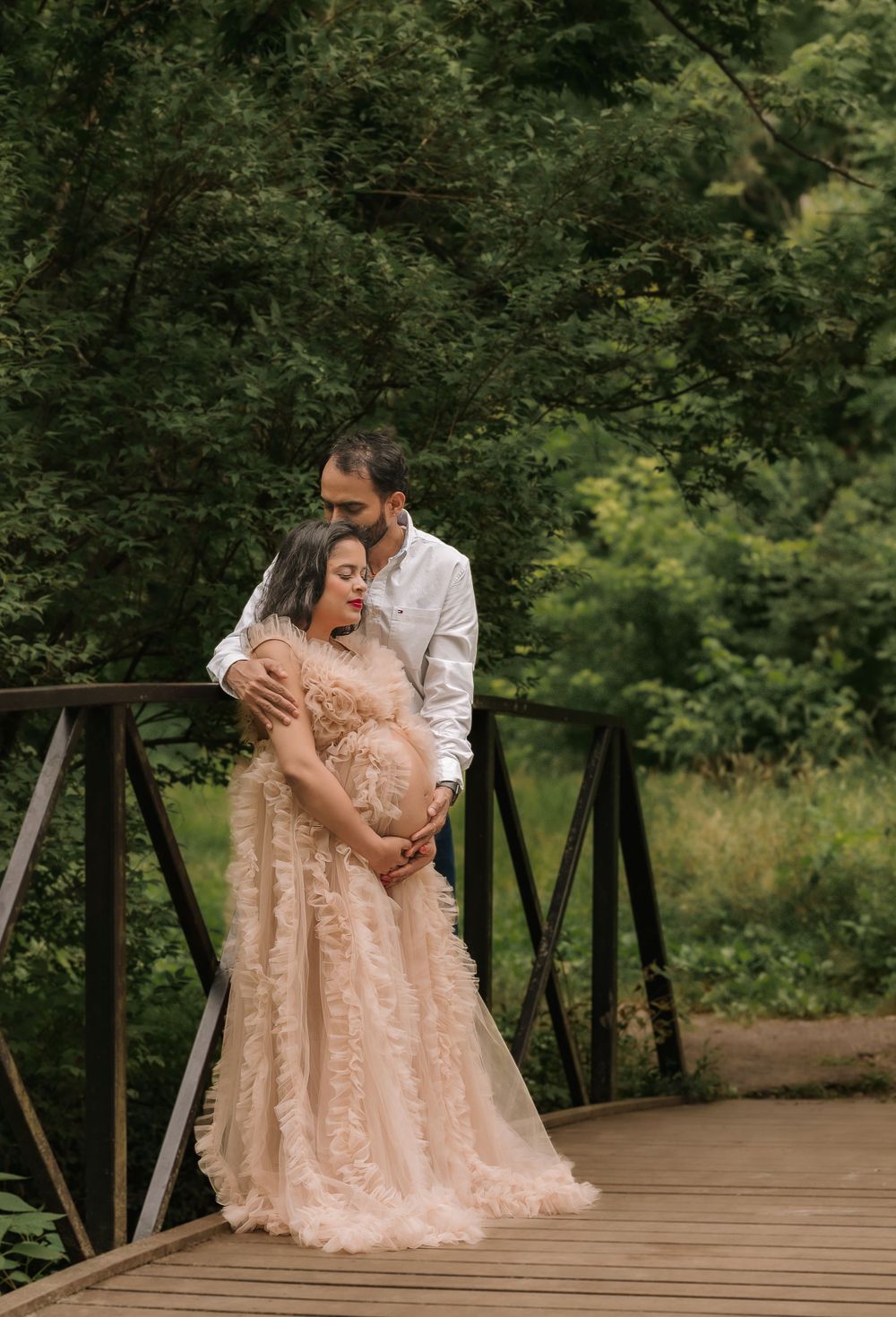 Romantic couple embracing on wooden bridge surrounded by lush green forest.