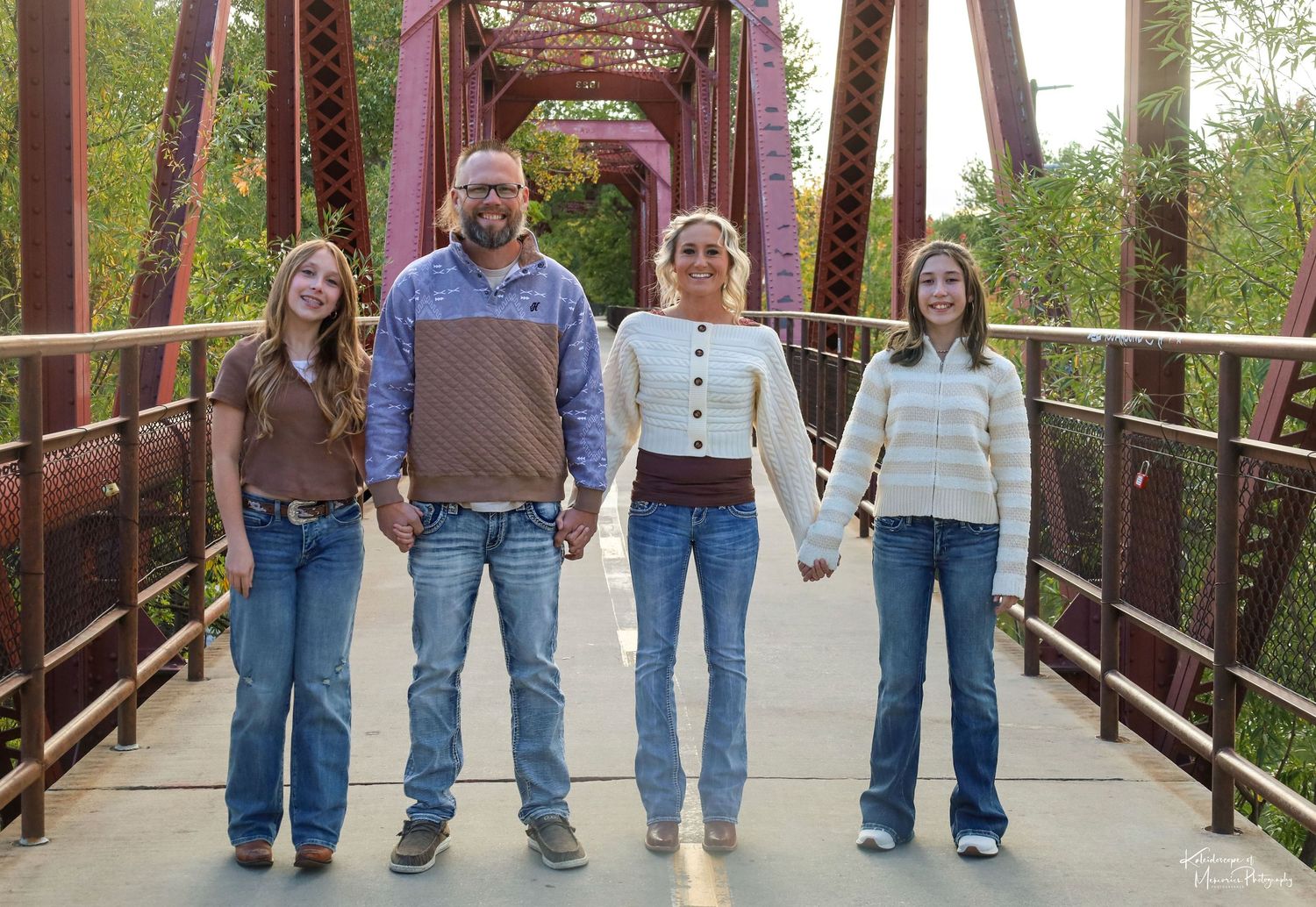 A group of people pose together outdoors with green foliage in the background.