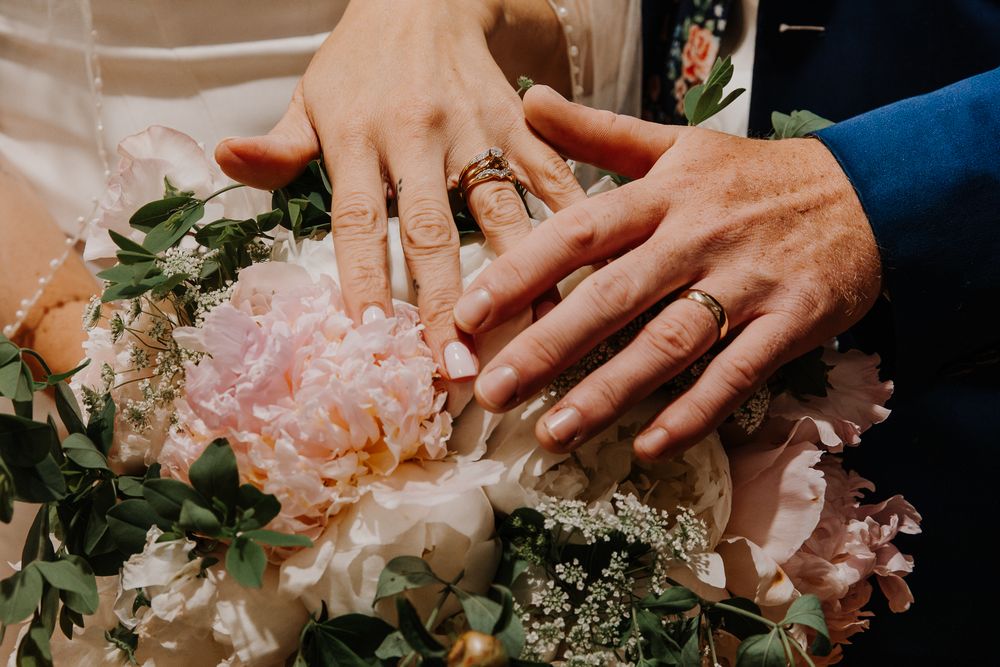 Close-up of hands displaying wedding rings surrounded by delicate pink flowers and greenery.