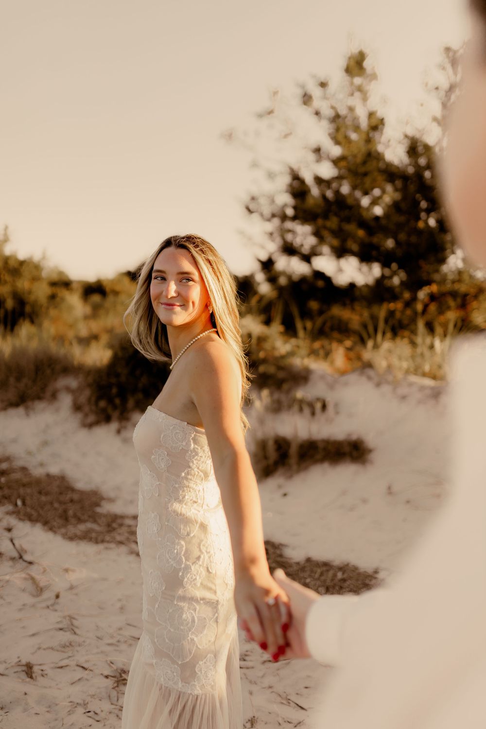 A romantic beach photoshoot at sunset with a white lace dress against sand dunes.