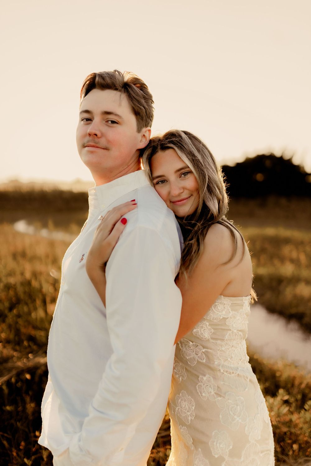 Couple in white clothing embrace tenderly on a beach during golden hour.