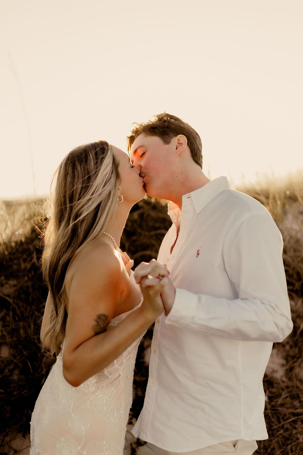 Loving couple in white share romantic kisses on the beach at dusk.