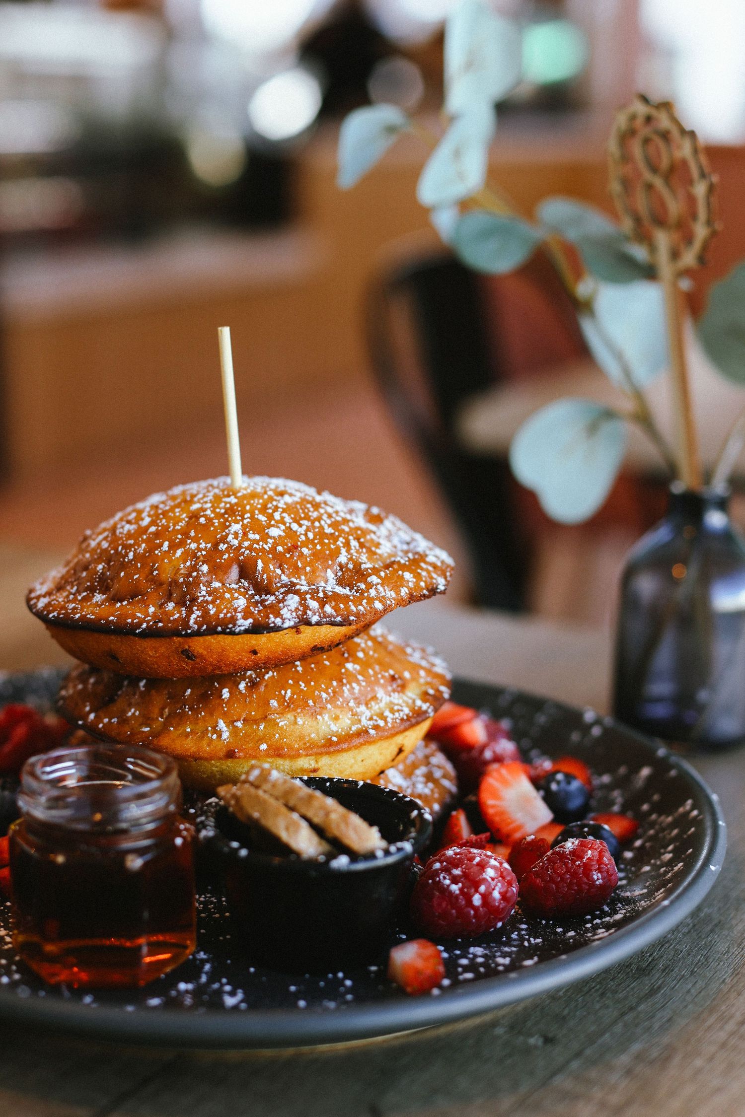 Stack of fluffy pancakes topped with powdered sugar, served with berries and syrup on a dark plate.