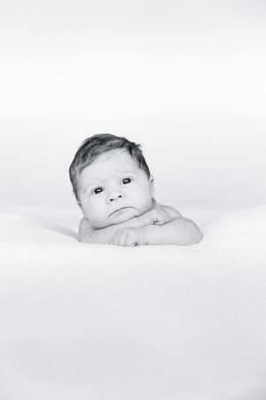 Black and white portrait of an alert newborn baby resting chin on hands looking up.