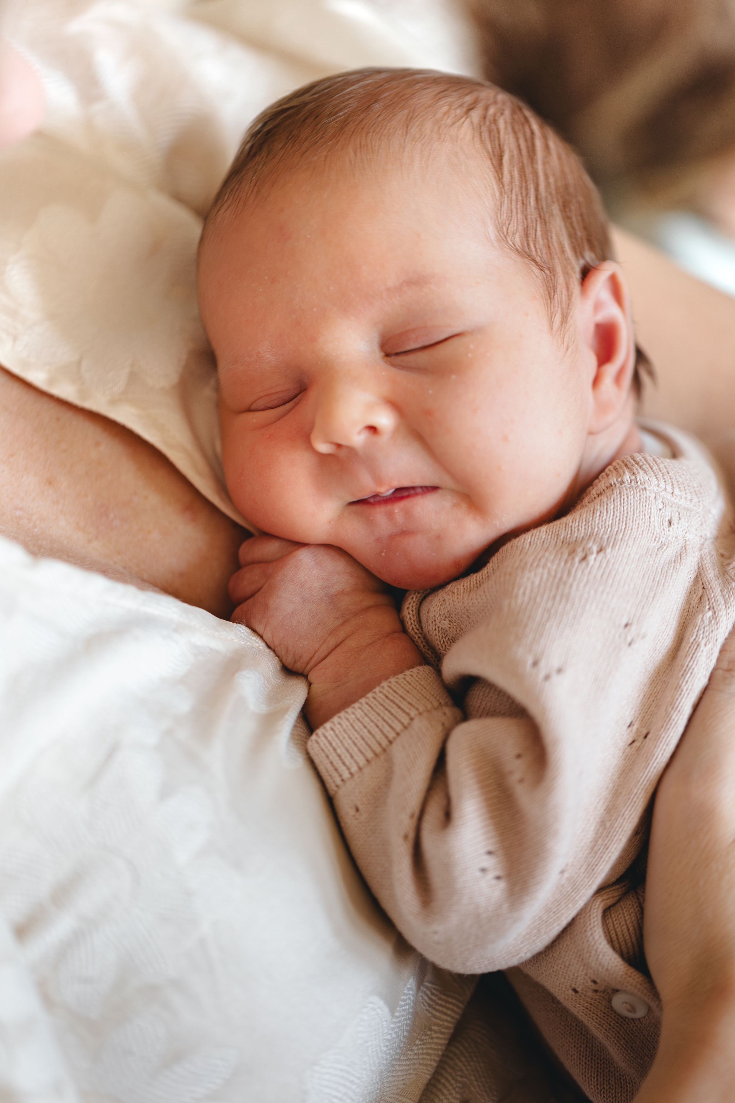 Peaceful newborn baby sleeping in parent's arms wearing a soft beige knit outfit.