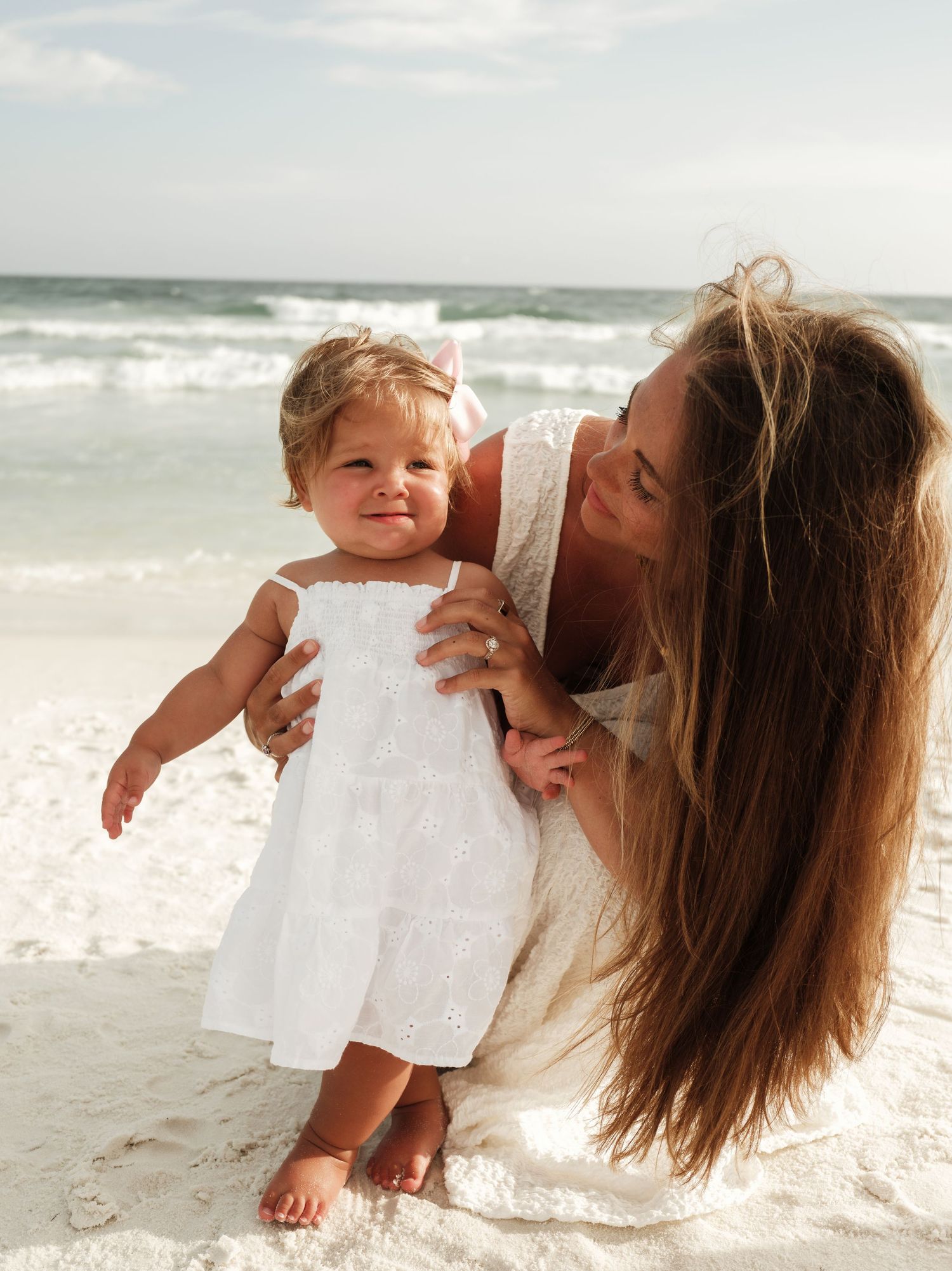 Mother and baby playing together on sunny white sand beach.