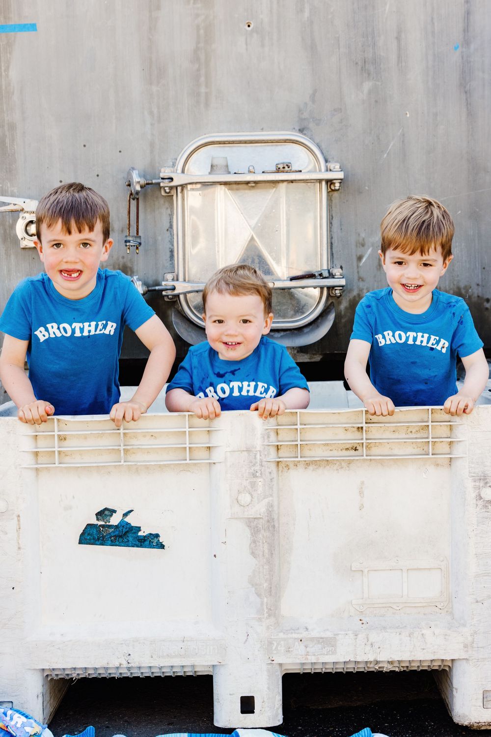 Multiple children in matching blue 'Brother' shirts lean over a white wall in a playful sequence.