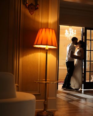 Couple sharing a romantic kiss in a doorway, framed by warm lamplight in an elegant golden-hued room.