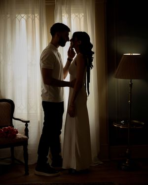 Romantic silhouette of a couple sharing an intimate moment by sheer curtains in a warmly lit room.