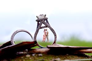 Creative wedding ring photo showing a detailed diamond engagement ring with a reflection of a couple standing inside.