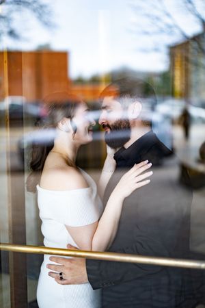 Couple sharing a romantic moment, photographed through a reflective glass window on a city street.