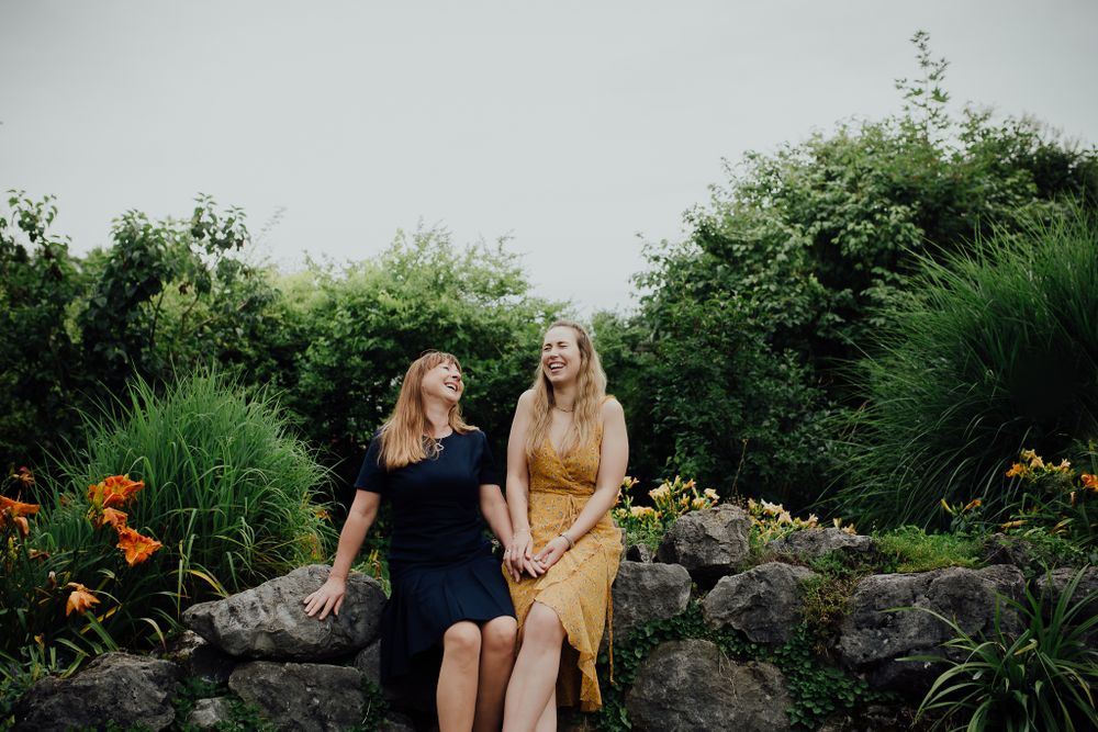 Zwei Personen sitzen zusammen auf Felsen in einem Garten, der mit grünen Pflanzen und orangefarbenen Blumen gefüllt ist.