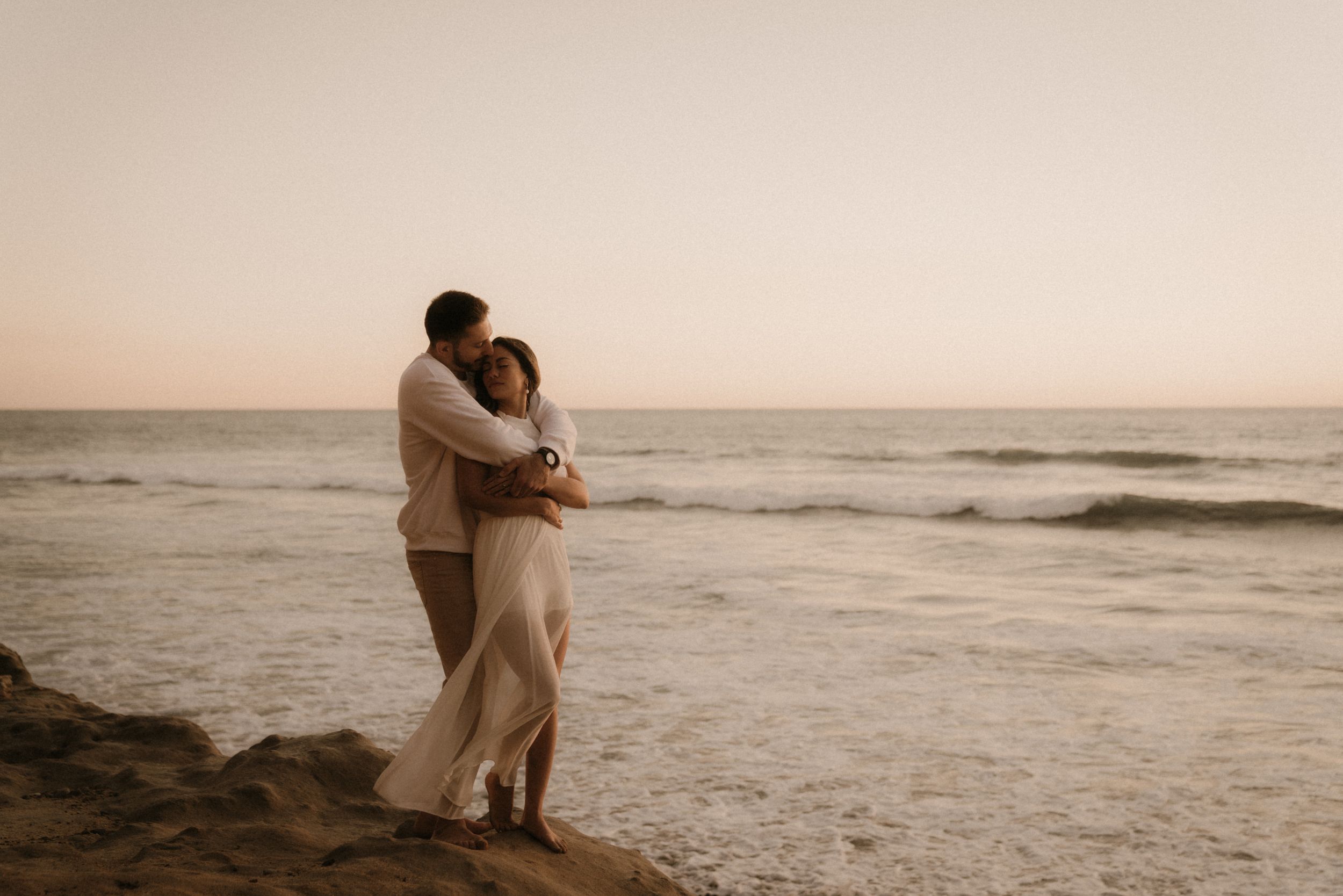 A couple embraces on a cliff overlooking the ocean at sunset creating a romantic silhouette.