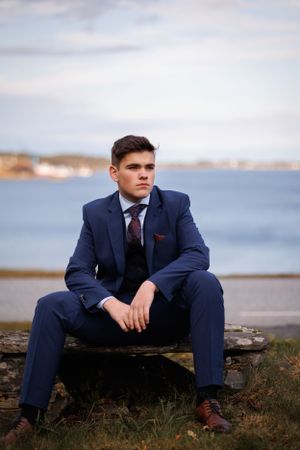 Formal portrait by the ocean featuring a tailored navy suit and burgundy tie.