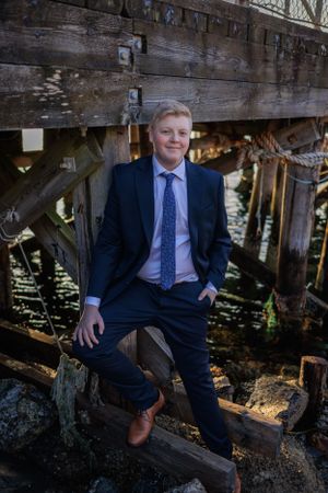 Professional portrait on weathered wooden dock wearing navy suit and light blue tie.