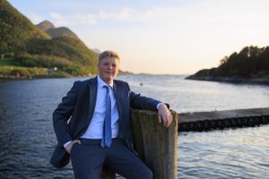 Professional portrait at sunset by a Norwegian fjord wearing a blue suit.