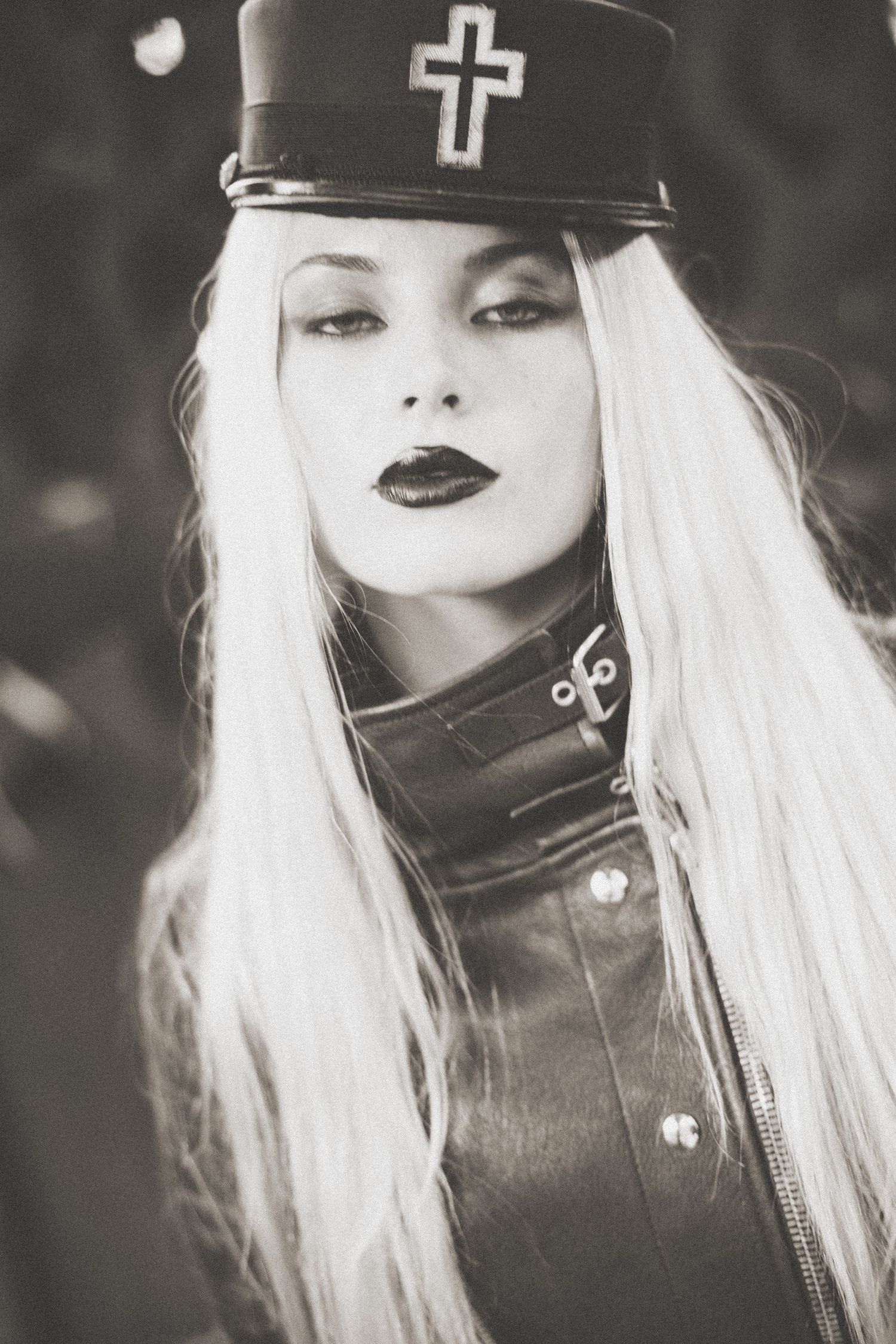 Black and white portrait showing dramatic gothic style with white hair, dark lipstick, leather jacket and cross cap.