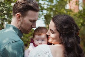 A tender family moment outdoors with a baby being embraced in a natural setting with greenery in the background.