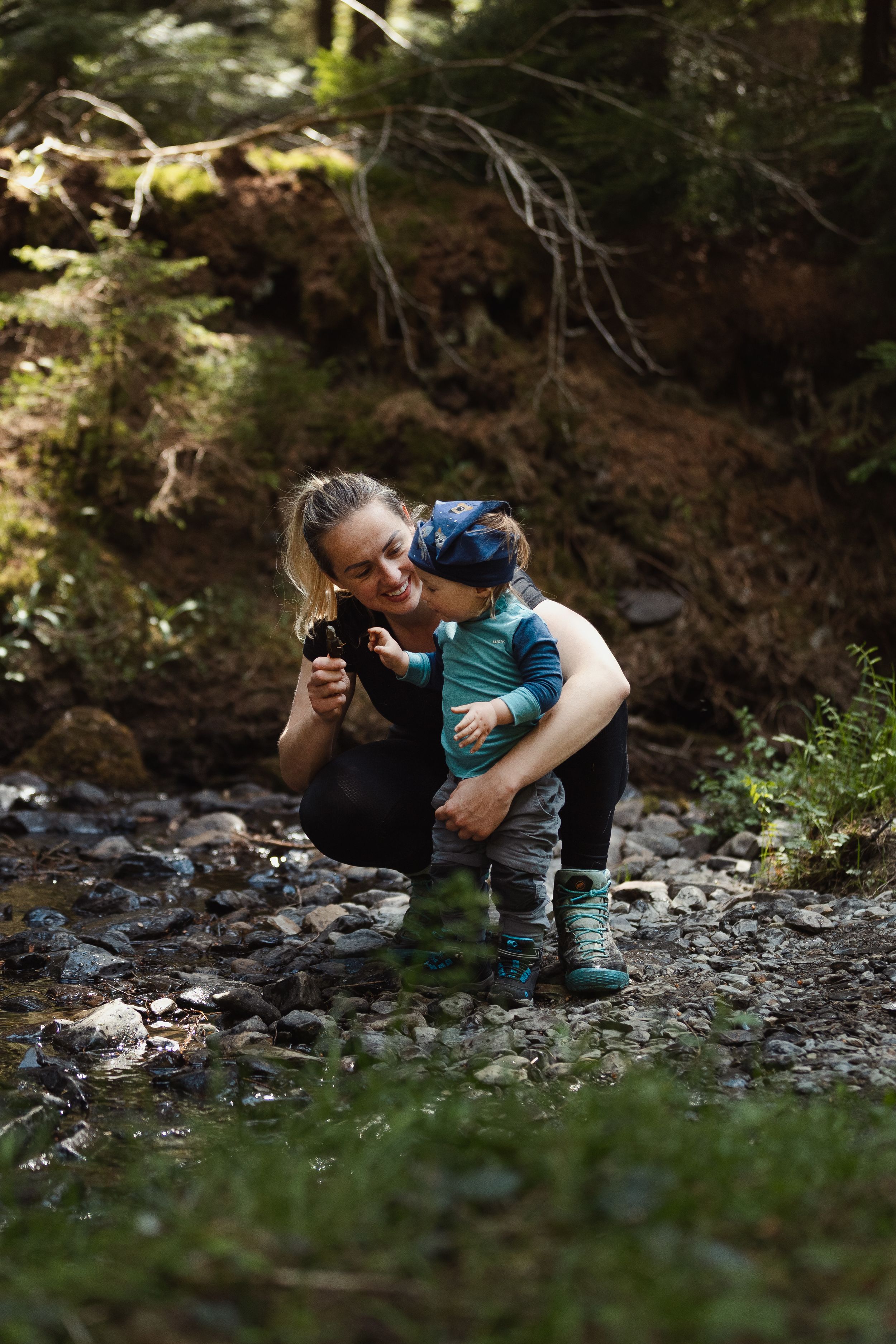 People exploring creek bed in forest while looking at something together.