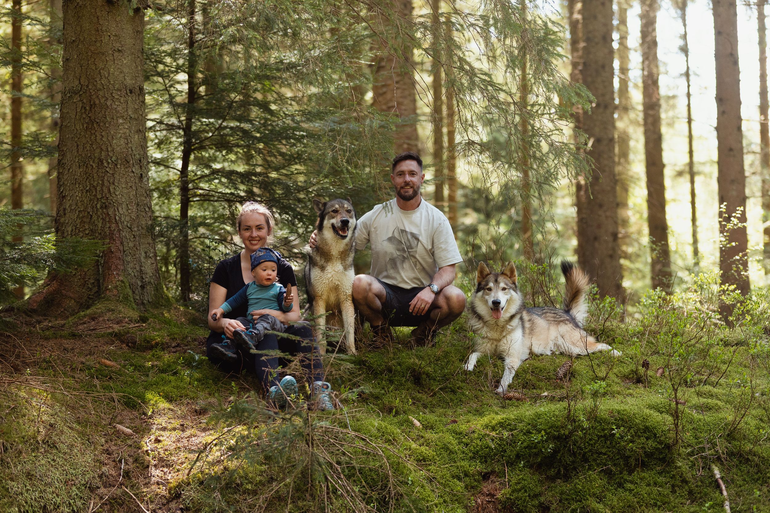 Family enjoying outdoor time with their dogs in peaceful forest setting.