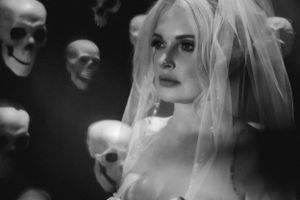 Dramatic black and white photo of rock 'n roll bride in a white veil with floating skulls in the dark background.