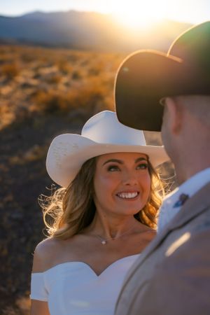 A couple in cowboy hats shares an intimate moment at sunset in a desert landscape.