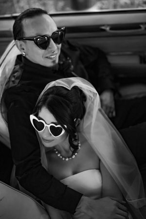 Retro black and white wedding photo of couple wearing matching heart shaped sunglasses in a vintage car at their Las Vegas elopement.
