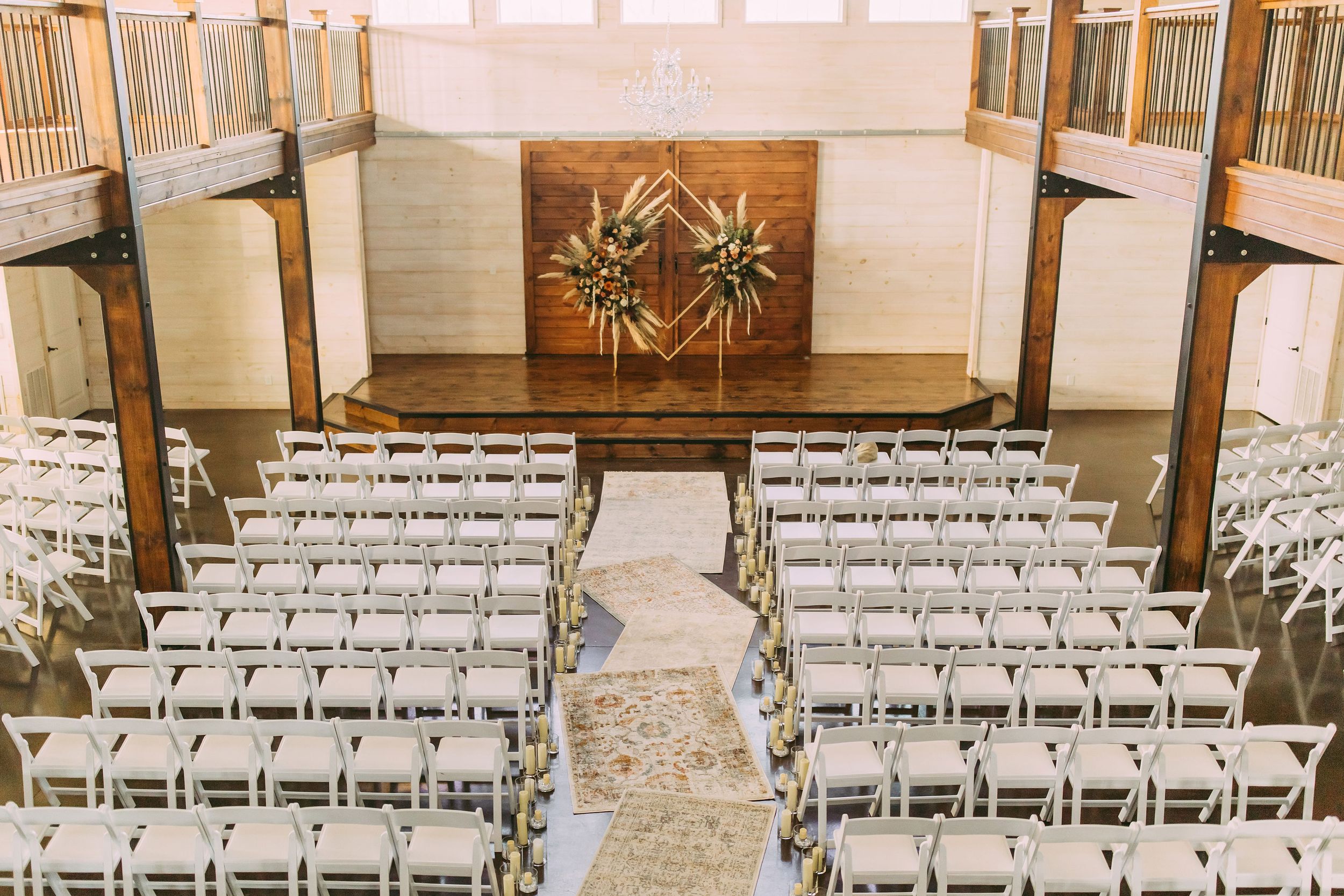 Wedding ceremony setup with white chairs and wooden geometric altar piece against white walls.