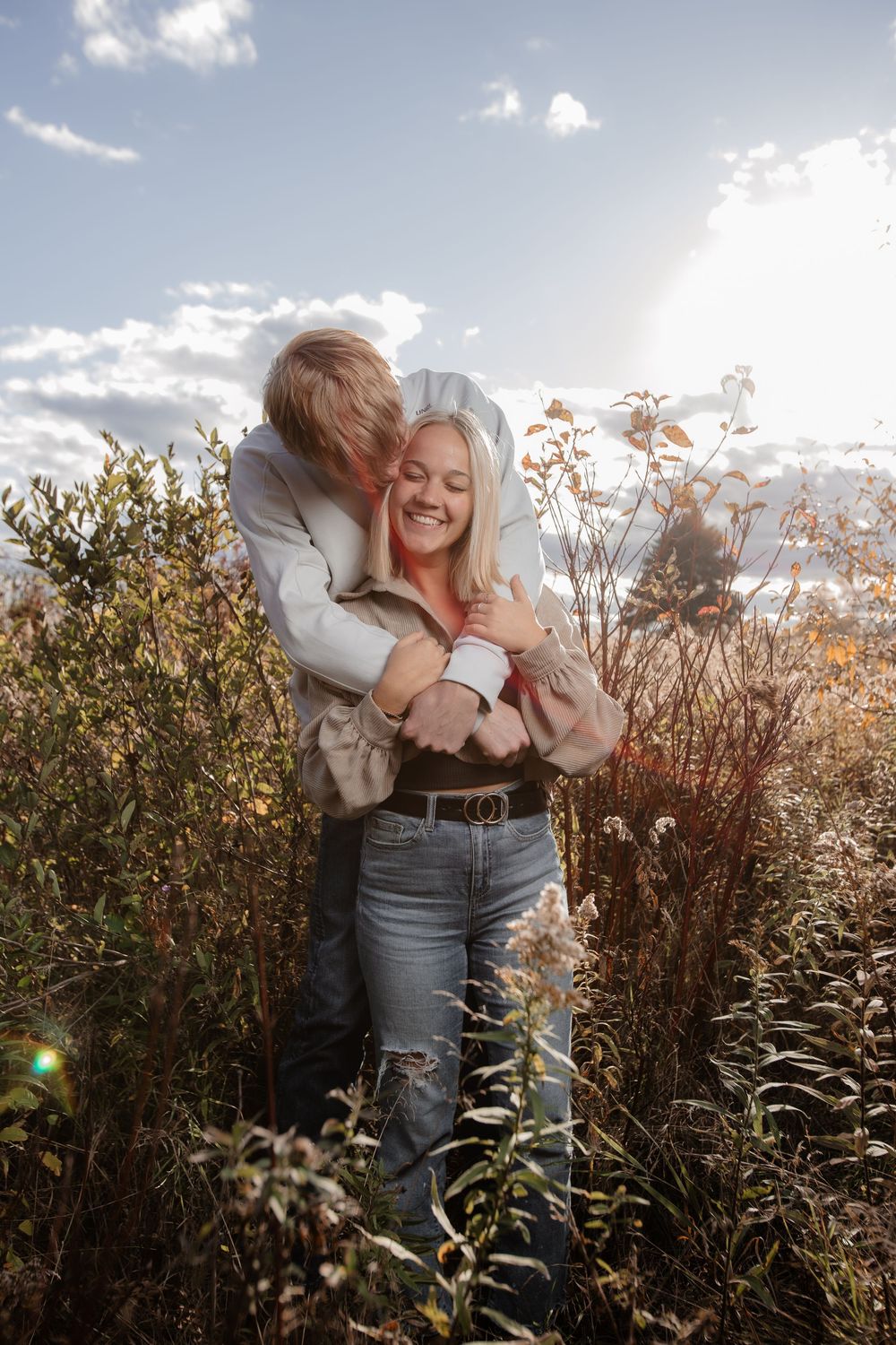 A romantic couple embraces in a field of tall grass during golden hour sunlight.