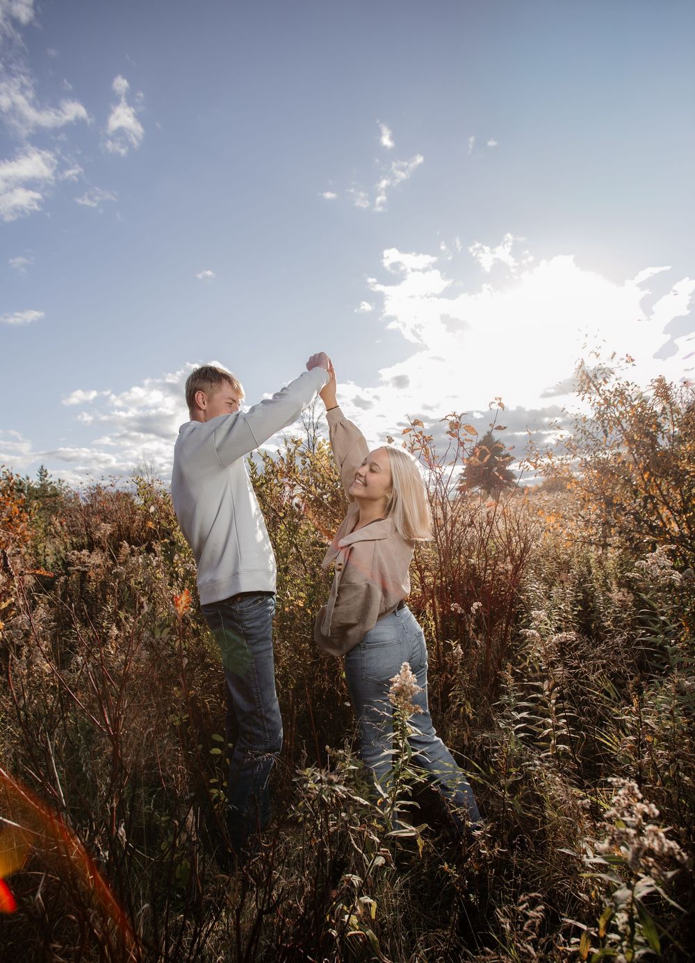 Couple dancing together in golden field during sunset with dramatic sky.