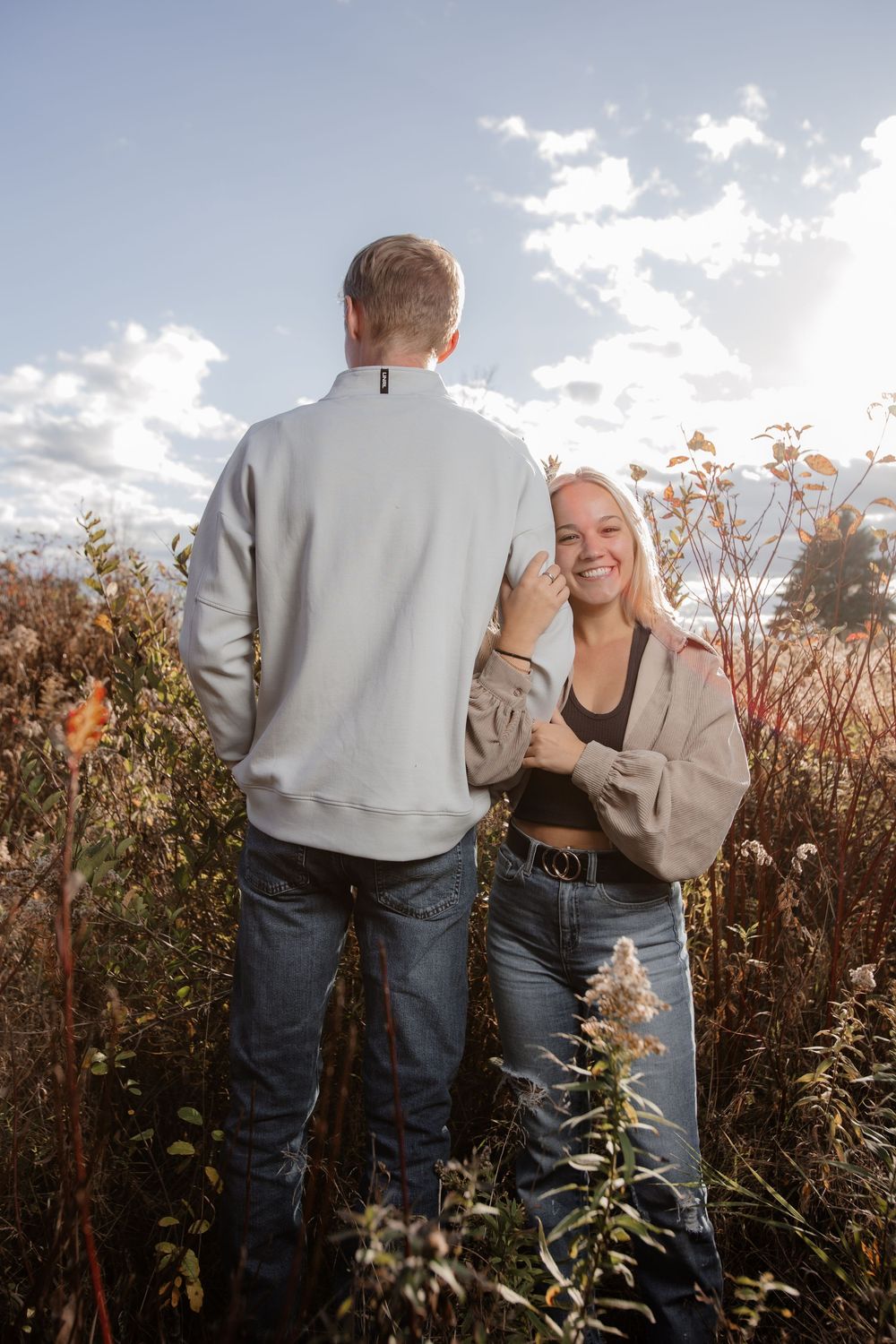 Couple sharing joyful moment in sunlit field with natural vegetation.