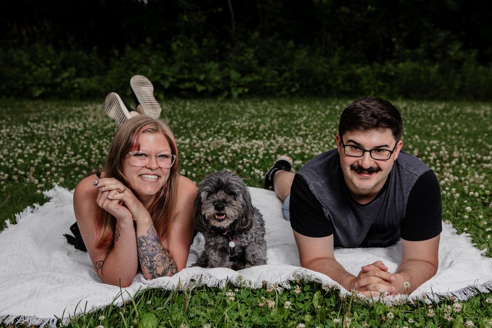 A couple poses with their small gray dog in an outdoor photoshoot series.