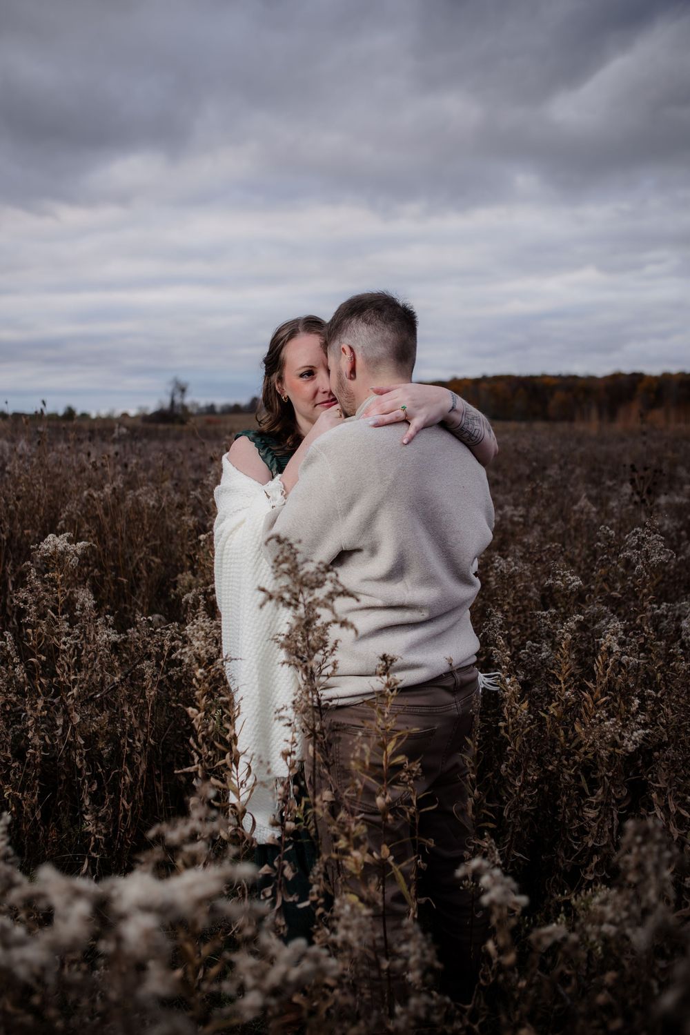Intimate engagement photos in moody field during overcast weather.