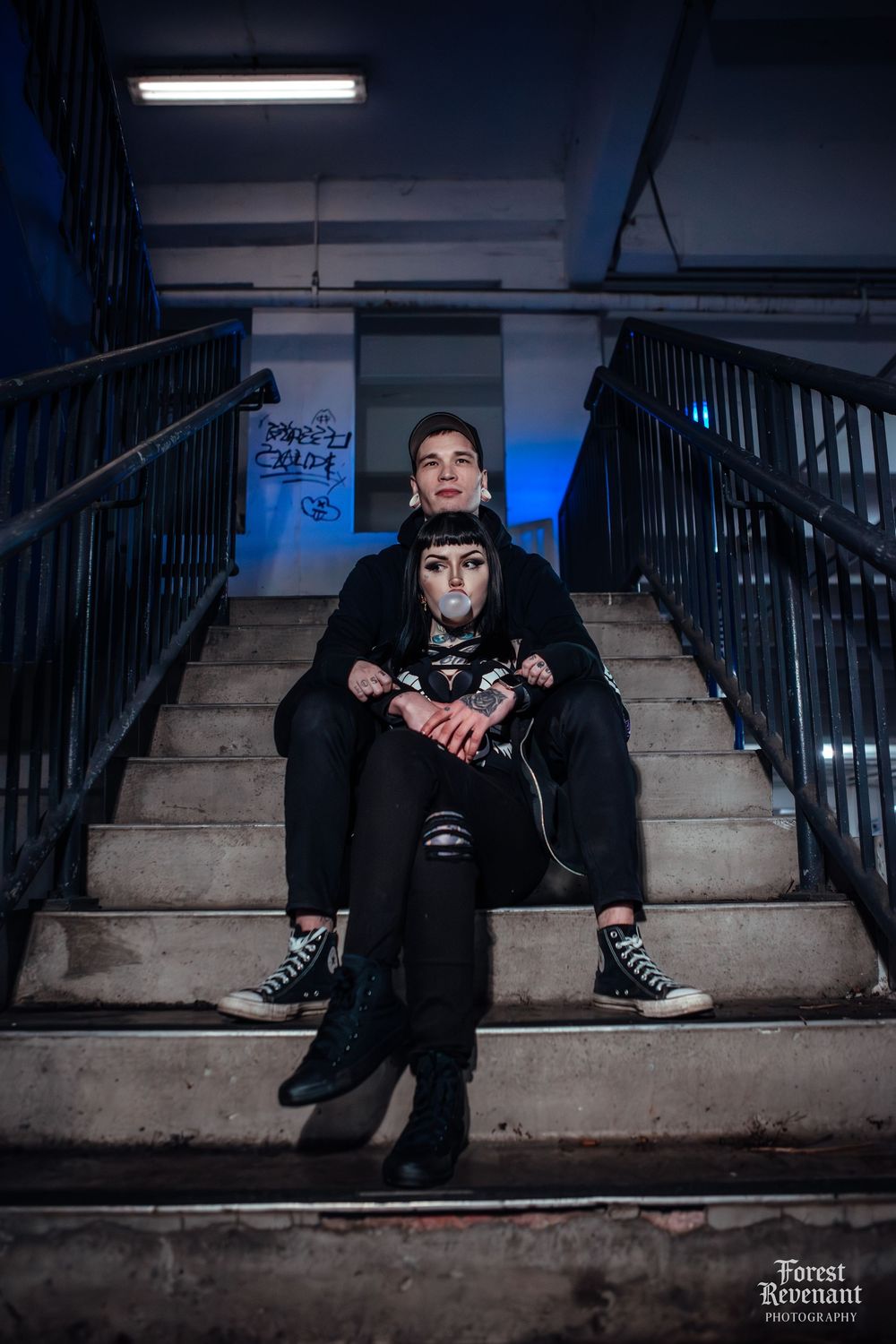Urban couple portrait on concrete stairs with blue lighting in an industrial setting (outside of a mall).