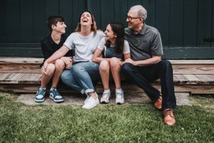 Four people sit together on wooden steps outdoors sharing a candid laughing moment.