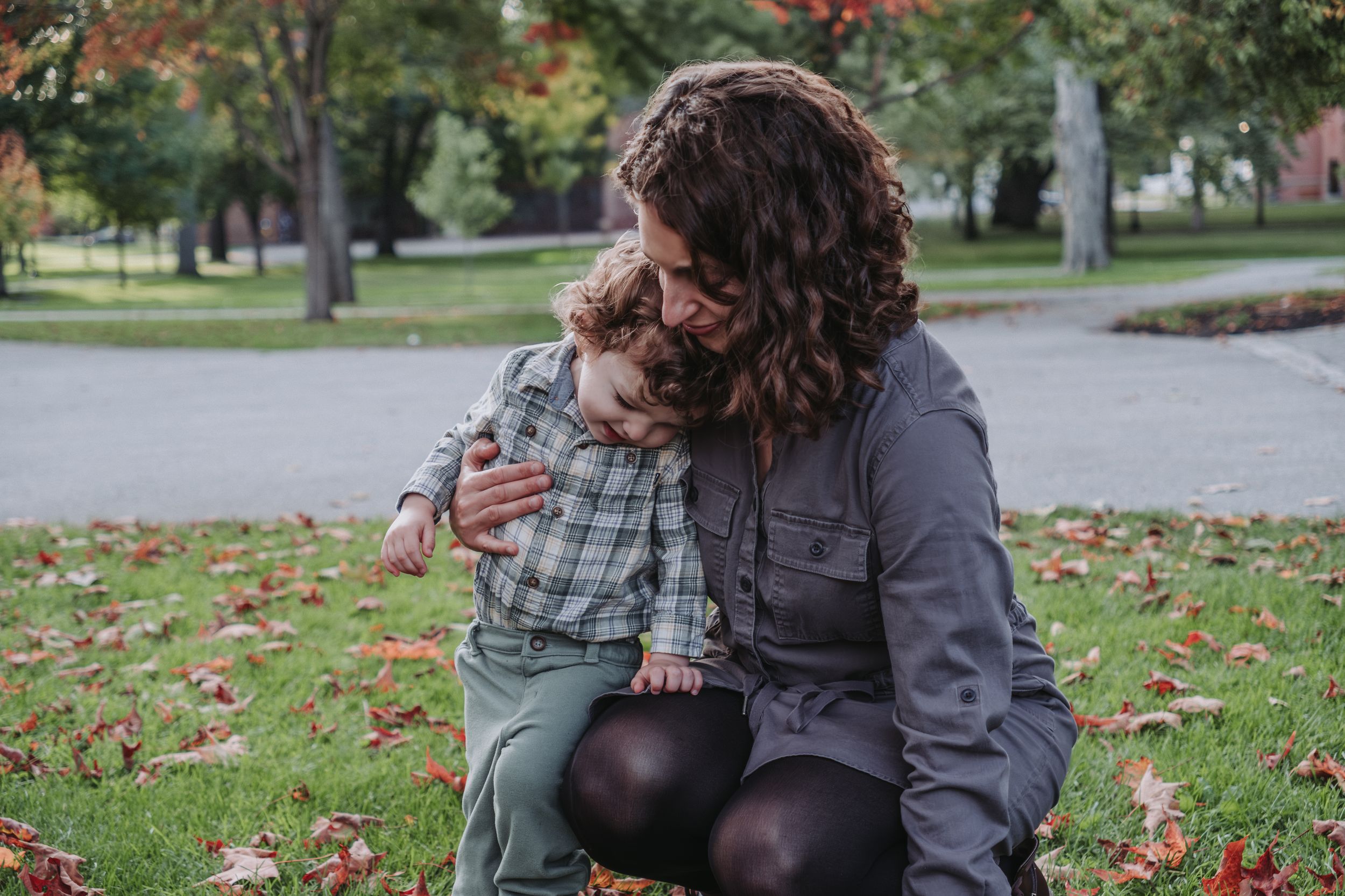 A parent and child share a tender moment while sitting on autumn leaves at Bowdoin College in Brunswick, Maine during a family session.