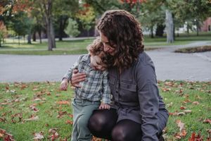 A parent and child share a tender moment while sitting on autumn leaves at Bowdoin College in Brunswick, Maine during a family session.