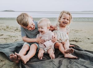 A brother smiles with a his little sister during a photo session at Popham Beach.  Their friend laughs next to them.