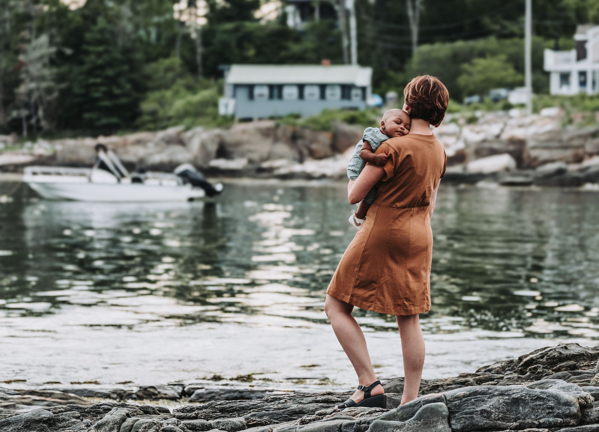 A mother holds her newly adopted baby while standing on beautiful, rocky shores at Ocean Point Park in Boothbay, Maine.