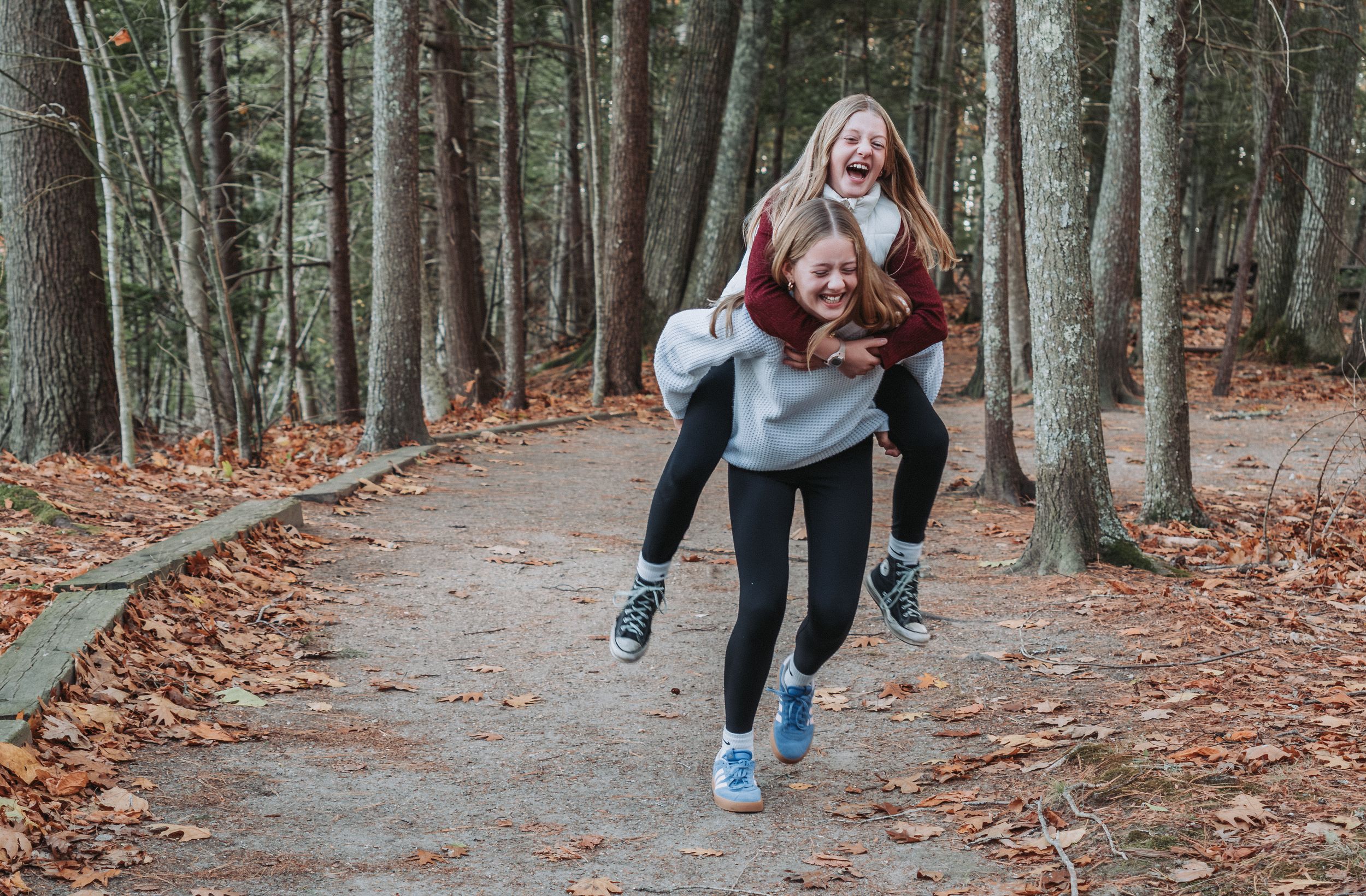 Two sisters enjoy a piggyback ride on a forest path through Wolfe's Neck State Park in Freeport, Maine.
