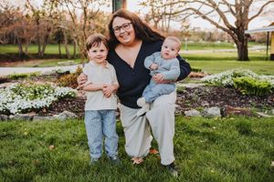A family stands together on green grass with blooming spring trees and flowers in the background.