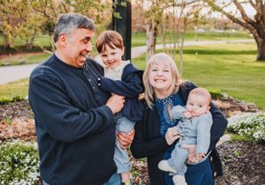 A joyful family moment captured outdoors in a park during autumn with blooming flowers in the garden.